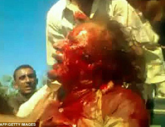 A handgun points at the head of Gaddafi who is facing the ground with his hands behind his back